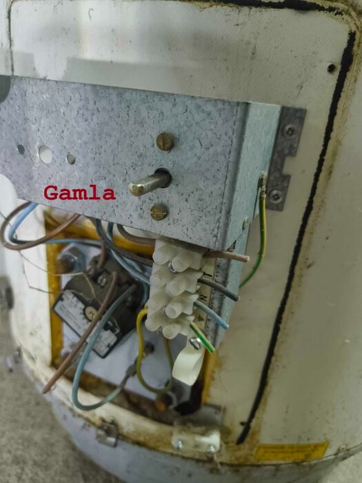 Gammal vattenberedare med elektrisk anslutning och kablar, märkningen "Gamla" syns vid en metallplatta.