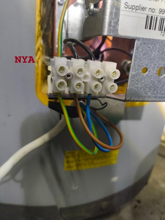 Kablar kopplade till en elektrisk kopplingsplint på en varmvattenberedare med texten "NYA" i bakgrunden.