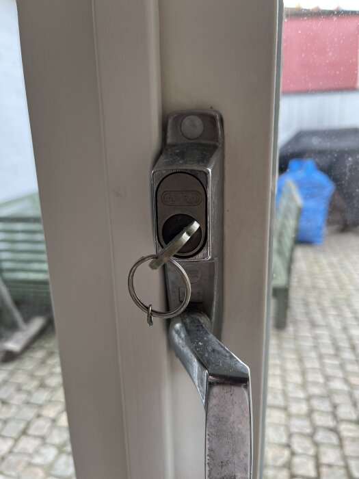 Nyckel i dörrlås med handtag, utomhusmiljö synlig genom fönster.