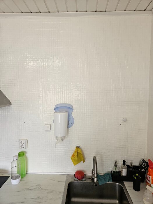 Köksvägg med kakel, diskho, handtvål, diskborste och hushållspapper på dispenser.