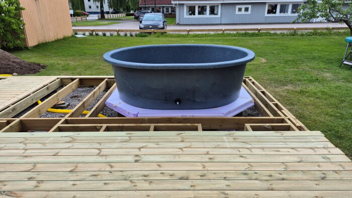 Utomhusprojekt med trästomme för terrasspool, visar en badtunna placerad på isolering över grus med trätrall under konstruktion i bakgården.