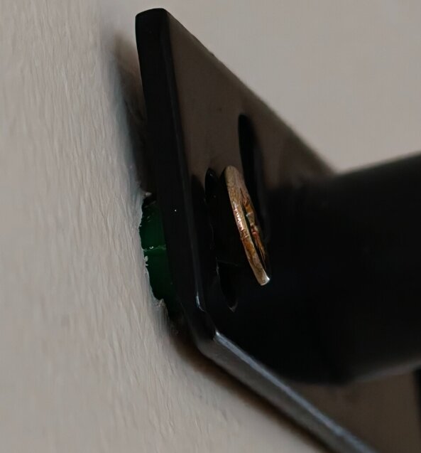 Närbild av en skruv som inte är korrekt använd i en svart metallinfästning på en vägg.