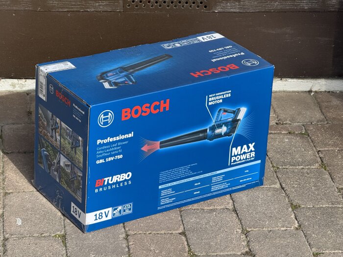 Kartong med Bosch sladdlös lövblås modell GBL 18V-750, Max Power, BIturbo Brushless, står utomhus på stenlagd yta.