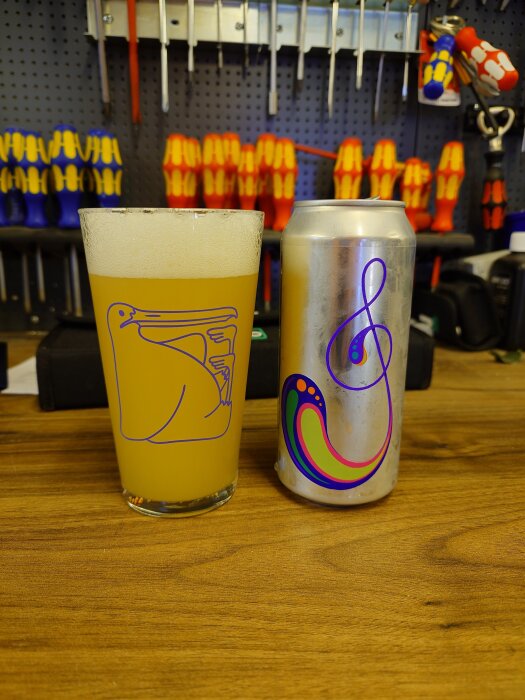 Ett glas öl från Omnipollo bredvid en burk med färgglad design, på en arbetsbänk i en verkstad.