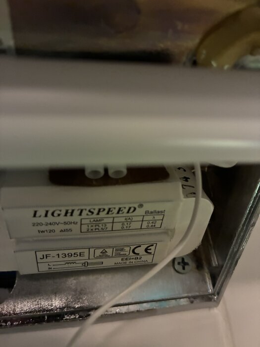 Närbild av en badrumslampa med en "Lightspeed" ballast märkt 220-240V 50Hz, modell JF-1395E, monterad i en metallram.
