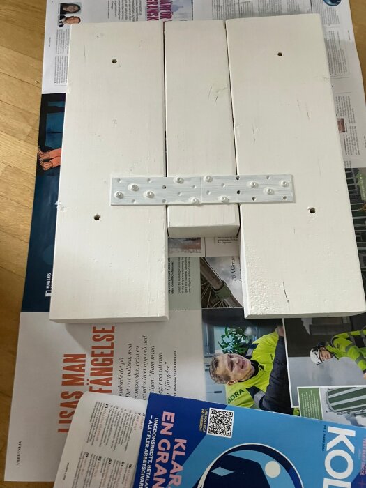 Träkonstruktion av vitmålade plankor på tidningar, del av racingpedalplattform, med metallbeslag i mitten, målad med ett lager snickerigrund.