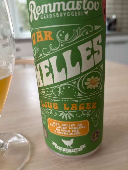 En burk Remmarlöv vår helles ljus lager på ett bord, med del av upphällt glas i förgrunden.