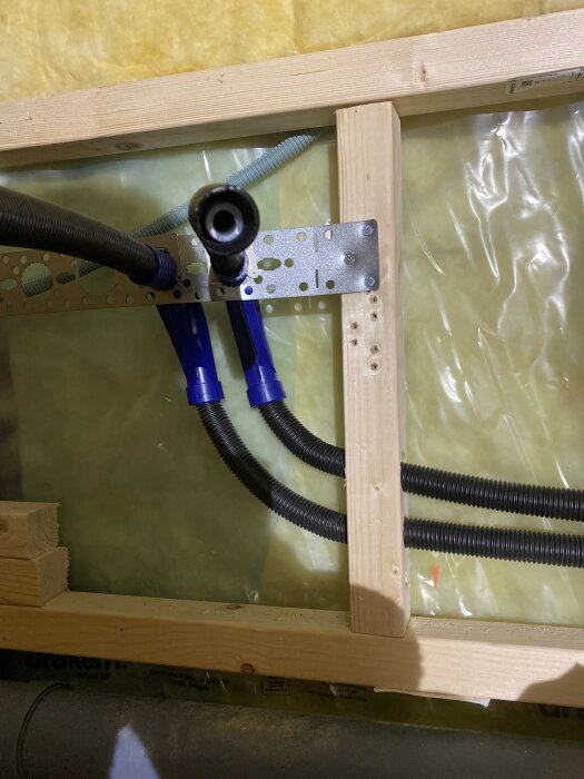 Bilden visar en installation av böjda rörsystem och PEX-rör, fästa vid en trästruktur med en metallhållare.