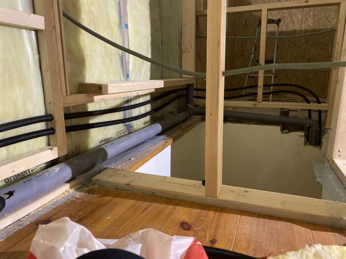 Träbalkar med isolering och installerade rör i ett rum under konstruktion.