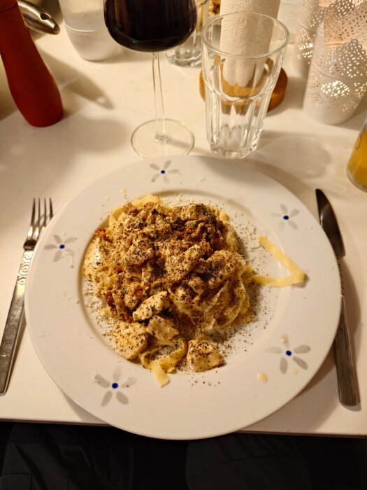 En tallrik med pastarätt toppad med kyckling och basilika, serverad vid ett dukat bord med rödvinsglas.