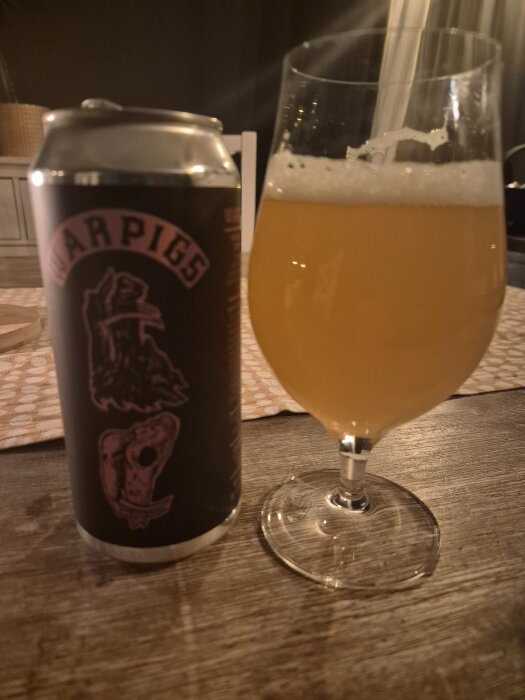 Burk med War Pigs-öl och ett glas med orangefärgad öl på ett bord.