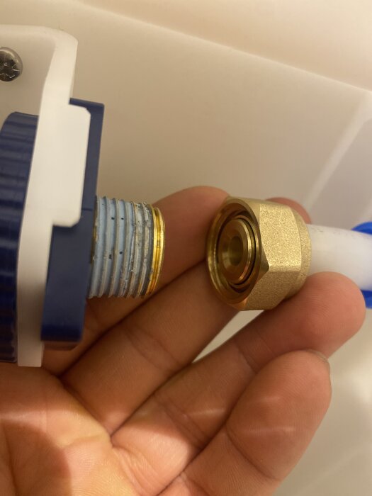 Hand som håller en blå och vit rörkoppling och en guldmässingsmutter redo för montering mot ett vitt bakgrundsmaterial.