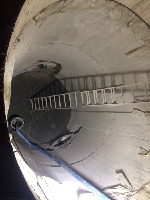Stor betongbrunn med stege och blått rör, används sannolikt för dränering eller som fördröjningsmagasin för dagvatten.