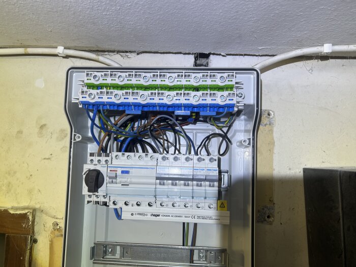 Elcentral med flera automatsäkringar och kopplingskablar installerad i ladugårdsvägg. Kablar och kopplingar är synliga i öppen enhet.