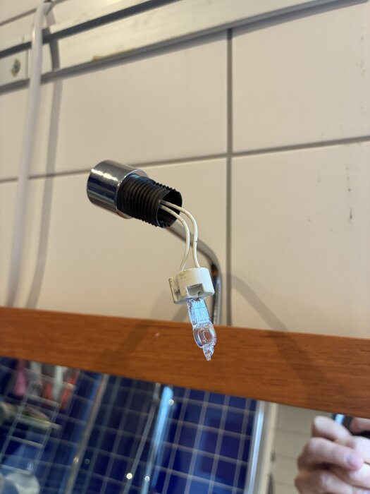 G4-lampa med vita sladdar ovanför badrumsspegel, delvis isatt i en vit plastsockel på kakelvägg, fungerar inte trots ström hela vägen.
