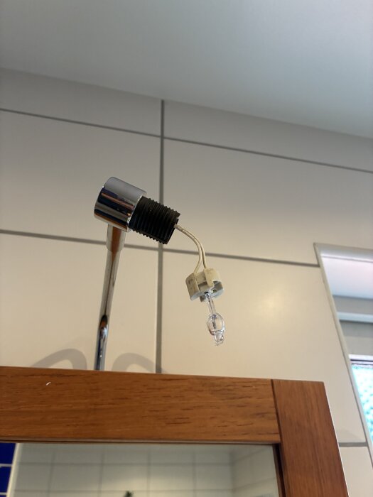 En G4-lampa hänger från en vit lampfattning ovanför en badrumsspegel i ett badrum med kaklade väggar.