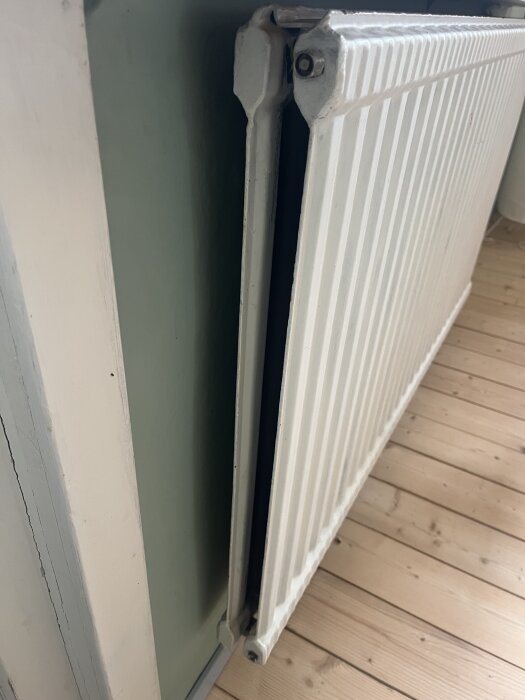 Vit radiator intill grön vägg och trägolv, sedd från sidan. Fråga om möjlighet att spegelvända inkopplingen av elementet.