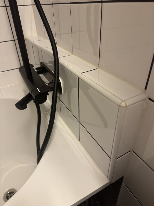 Duschblandare monterad på kaklad nisch i badrum med synliga monteringsfel och otillräcklig tätning, svart duschslang installerad.