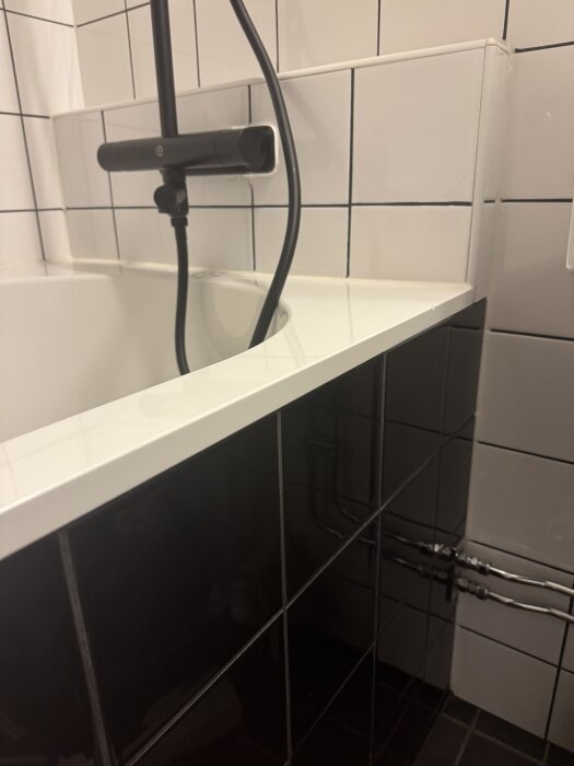 Svart duschblandare monterad på kakelvägg, kopplad till rör. Installation verkar läcka, monterad på tidigare byggd nisch ovanför badkaret.