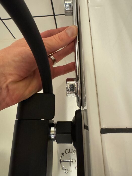 Närbild på en hand som håller i en duschslang och duschblandare installerad på en nisch med läckageproblem, rör syns.