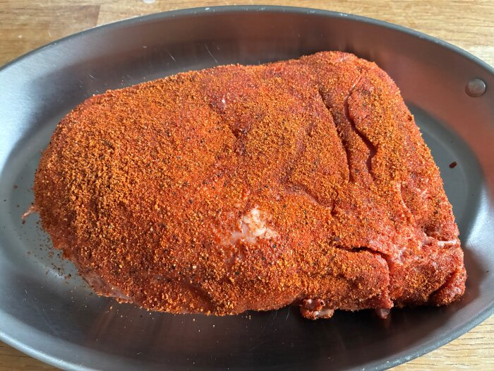 Köttstycke täckt med kryddrub i en grillform, redo för grillning eller rökning.