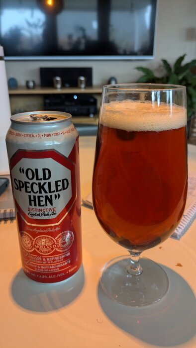 En burk Old Speckled Hen öl bredvid ett glas med brunfärgad öl på ett bord.