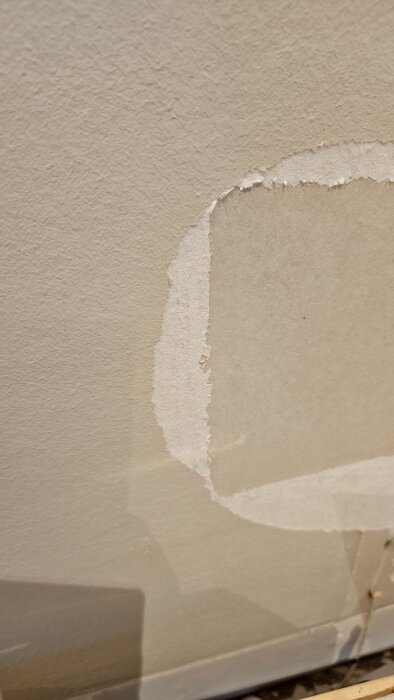 Bilden visar en vägg där gammal garderob tagits bort, avslöjande vit fiberduk och ett underliggande, jämnt grått skikt.