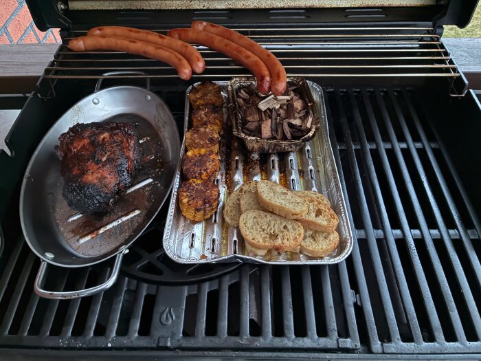Grill med köttbit, korvar, majskolvsbitar, rökträ i folieform och skivor av bröd.