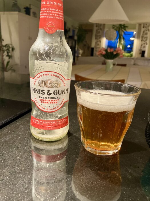 Flaska och glas med Innis & Gunn öl på ett bord, i bakgrunden syns ett rum med blommor och inredning.