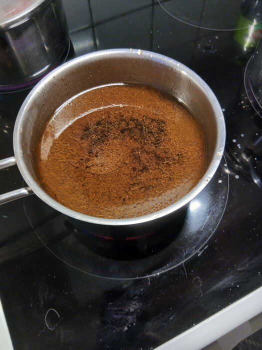 Kastrull med brun vätska som kokar på en mörk spishäll i ett kök.