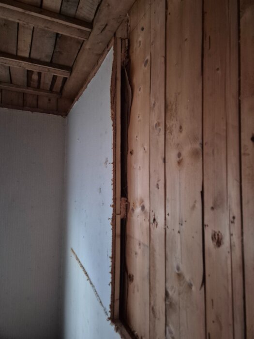 Sektion av yttervägg med stående plank och skikt av borttagen panel, visar konstruktionens inre skikt och taket ovanför.