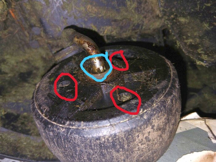 Närbild på ett gräsklipparhjul med axel, där blå ring markerar axelstopp och röda ringar visar försänkningar för skruvar.