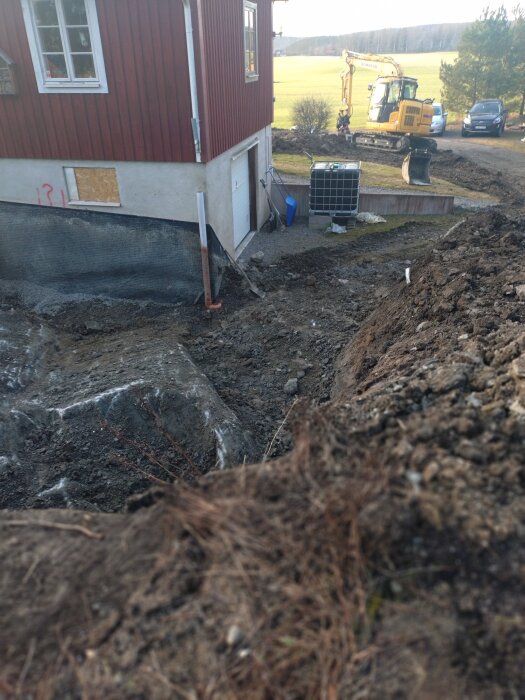 Grävmaskin vid utbyggnad av hus med grävad mark och sprucken betong, inga växande ogräs synliga.
