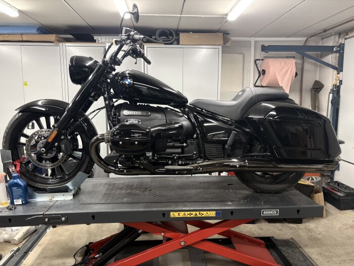 Svart motorcykel på lyft i ett garage med verktyg och förvaringsskåp i bakgrunden.