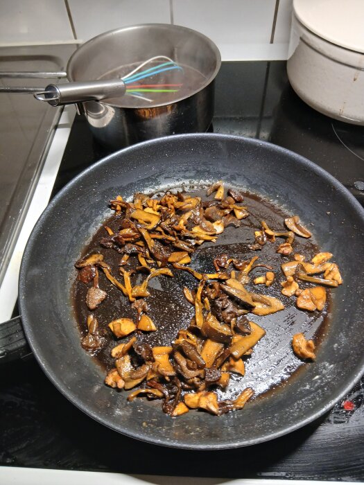 Stekta blandsvampar i stekpanna på spis med kastrull i bakgrunden som innehåller visp för potatis- och palsternackspuré.