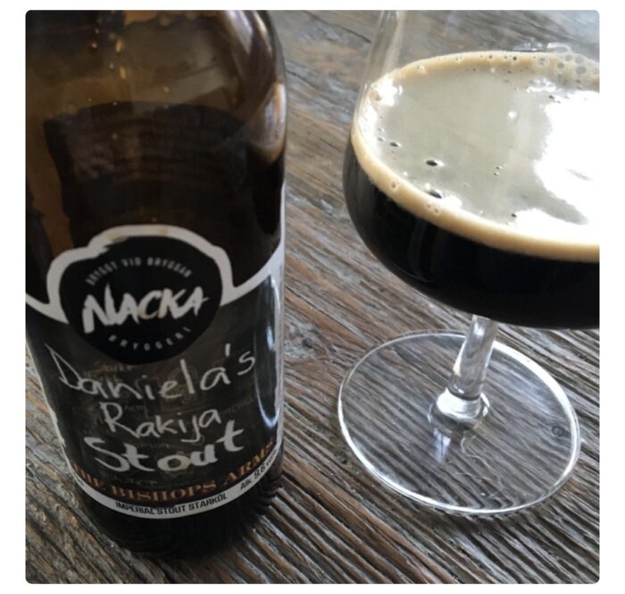 Flaska Daniela's Rakija Stout och ett glas fyllt med stout på ett träbord.