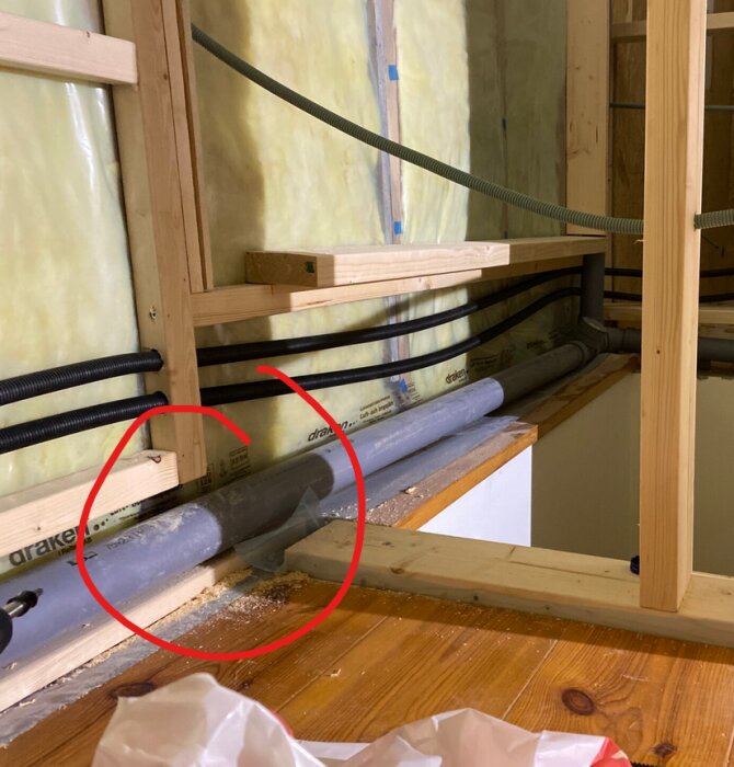 Byggvägg med oskuren bockfixtur som sticker ut, träregel, rör och isolering synliga, markerat med röd cirkel.