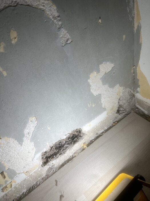 Gipsvägg med skador och ett hål som exponerar sågspån eller isoleringsmaterial, tagen under renovering av en lägenhet från 1954 i Stockholm.