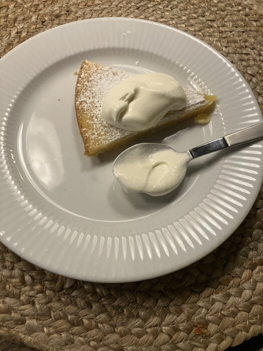 En bit citronkladdkaka med grädde serverad på en vit tallrik med sked.