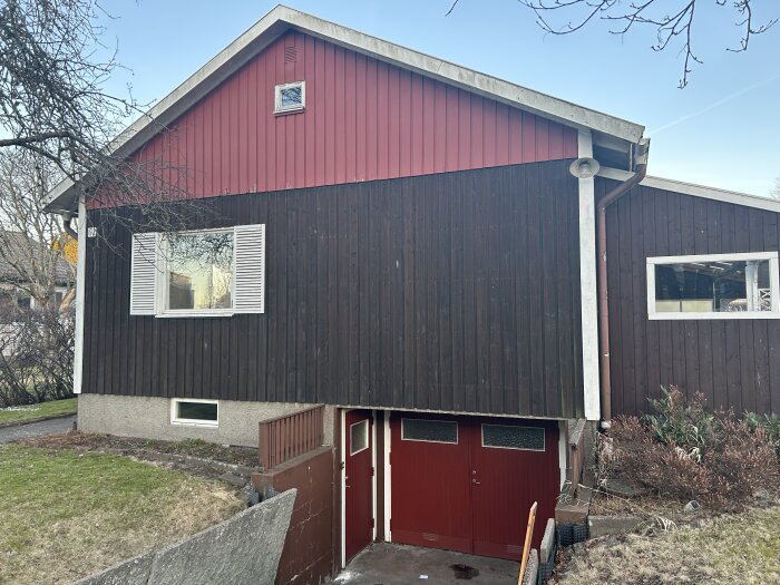 Fasad av ett hus med brun och röd träpanel som ska renoveras, veranda ska rivas. Fasad bakom verandan uppges vara i relativt gott skick.