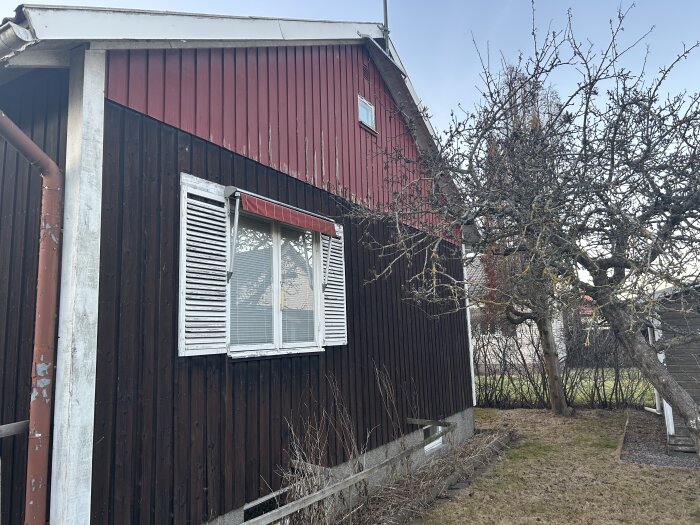 Brunmålad fasad med vita fönsterluckor och sprucken färg, framför ett naket träd och en liten veranda som ska rivas.