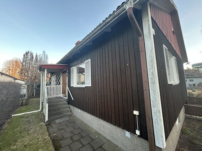 En äldre veranda med vitmålat räcke ses framför en brun fasad som är i gott skick, med fokus på trappan och kortsidan.