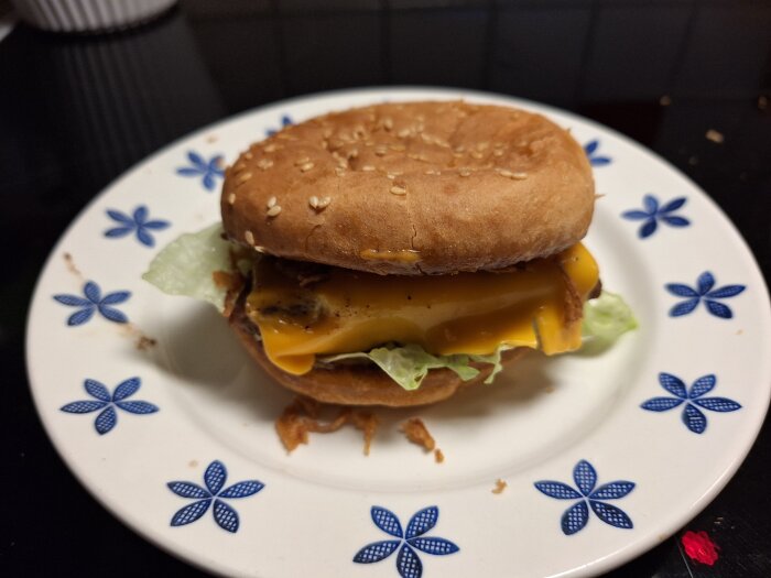 Hemmagjord hamburgare med sallad, ost och rostad lök på en tallrik med blommönster.