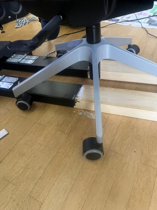 Målad bas med fastskruvade pedaler, stol på hjul, 2x4 träregel monterad för att stödja stolens fäste i ett byggprojekt.