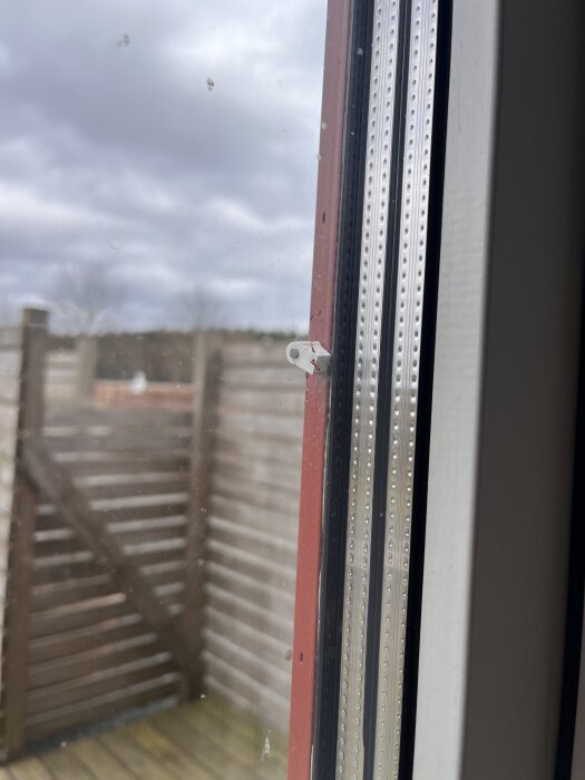 Röd-målad plastspreJs fästad med klick-fäste i fönsterkant, utomhusmiljö i bakgrunden.