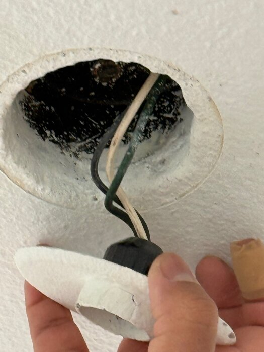 En hand håller en lamphållare med synliga elektriska ledningar från taket.