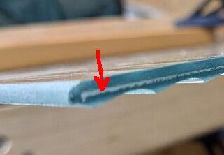 En närbild av kanten på ett platt material med en röd pil som pekar på en definierad kant eller lager i materialet.