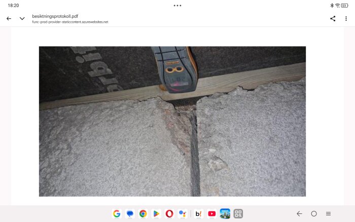 Fuktmätare som visar värde placerad på trä i krypgrund med synlig skada och dammiga boardskivor.