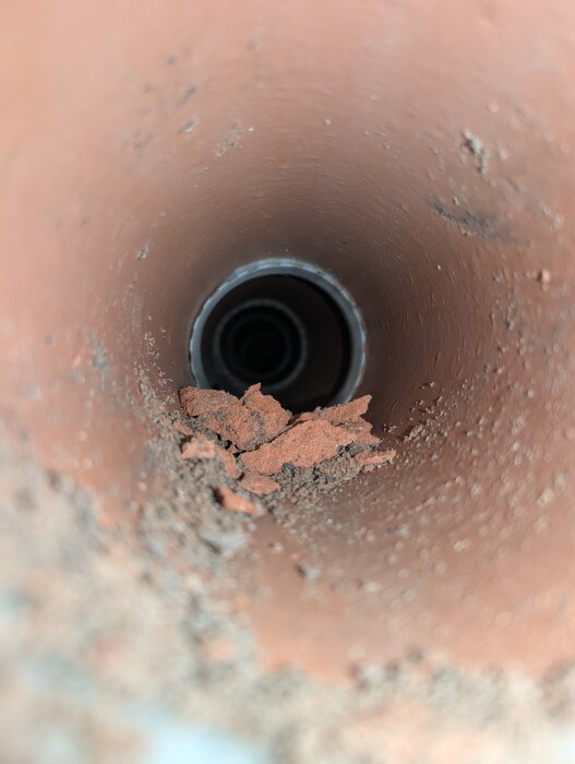 Utsikt inuti ett äldre, torrt tegelrör med plastmuffar, delvis fyllt med jord och smuts, upptäckt under grävning för eldragning.