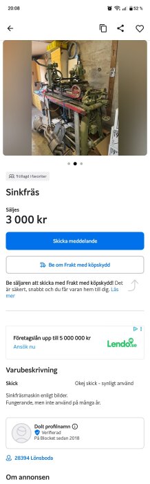 En gammal sinkfräsmaskin stående i ett verkstadsrum med verktyg och hyllor i bakgrunden.